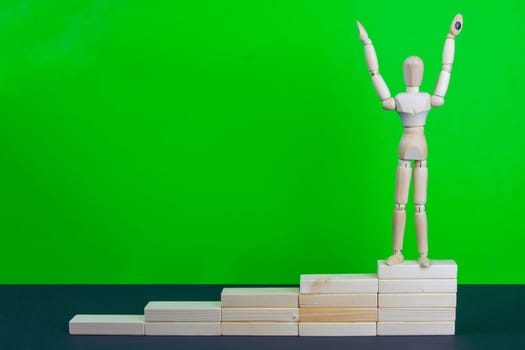 Wooden man walk up the career stairs. Ladder made with wooden bricks. Mannequin on top of development. Concept of personal development, career , changes, success. Green background, copy space for ad.
