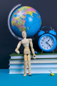 The globe and the clock stand on a stack of books, next to a glass of pencils and the pyramid is folded with wooden cubes and the figure of a wooden man.