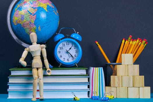 The globe and the clock stand on a stack of books, next to a glass of pencils and the pyramid is folded with wooden cubes and the figure of a wooden man.