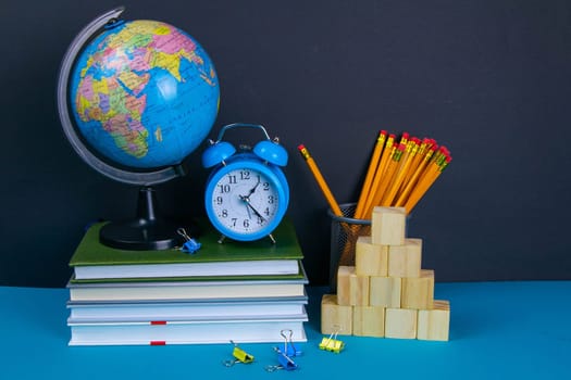 The globe and the clock stand on a stack of books, next to a glass of pencils and the pyramid is folded with wooden cubes.