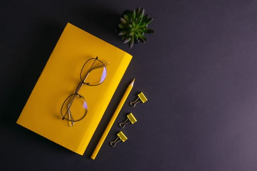 Yellow pencil, yellow notebook and glasses, pins, clip paper on on black background.