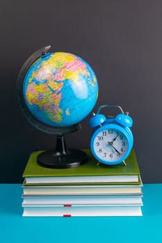 The globe and clock stand on a stack of books, on a blue table.