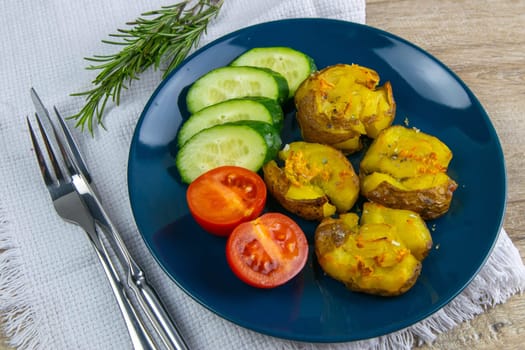 Baked potatoes with cheese, and salad with tomatoes and cucumbers on a blue plate.