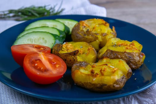 Baked potatoes with cheese, and salad with tomatoes and cucumbers on a blue plate.