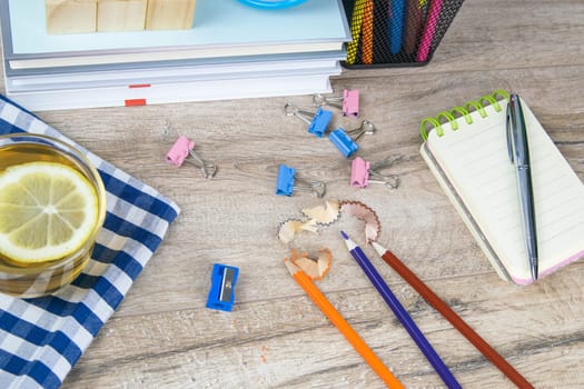 A stack of books, a clock, wooden cubes in the shape of a pyramid, next to there is tea with lemon in a transparent glass glass and multi-colored pencils.