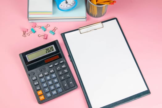 On the pink table there is a calculator and a tablet with a white sheet, next to sprinkled clothespins for paper.