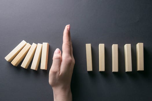 Top view whomen hand stopping falling dominos in a business crisis management conceptual image.