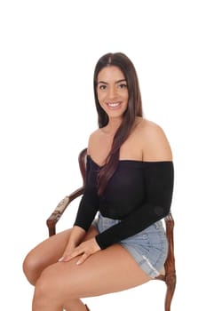 A gorgeous young woman sitting in a old armchair for a portrait, in.shorts and black top, isolated for white background.