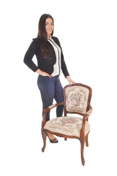 A gorgeous caucasian woman in jeand and a black jacket standing.with an old armchair, isolated for white background.