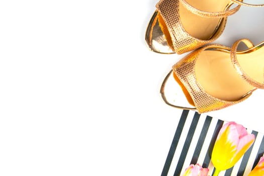 Golden women's shoes together with tulips on a white background.