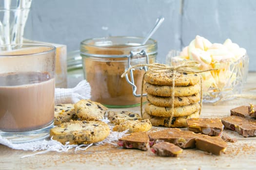 Spicy hot chocolate with cinnamon stick and chocolate chip cookies over wooden background.