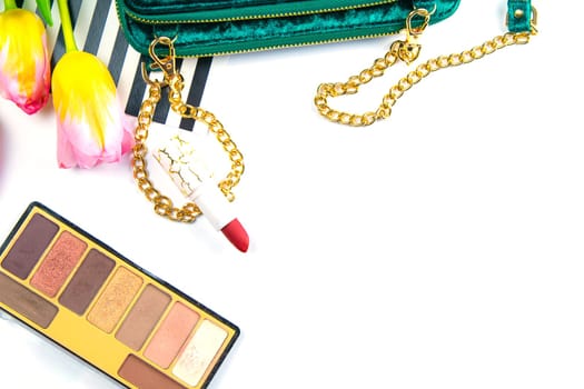 Tulips with green women's clutch, pallet with shadows and women's cosmetics on a white background.