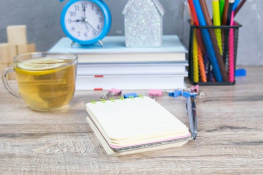 An open notebook on a wooden table, next to stand a silver pen and a cup of mint tea with lemon.