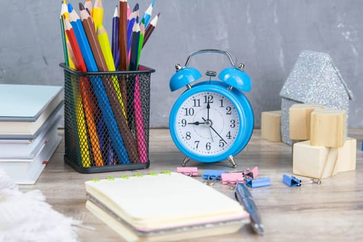 A stack of books, a clock, wooden cubes in the shape of a pyramid, next to there is tea with lemon in a transparent glass glass and multi-colored pencils.