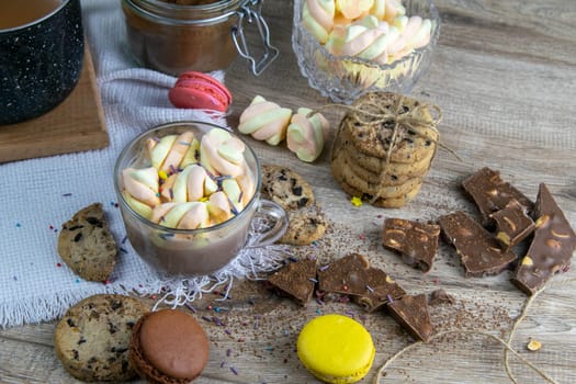 Cocoa with marshmallows and chocolate oven, muffins and chocolate slices stand on wooden table.