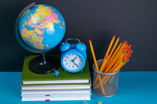 The globe and the clock stand on a stack of books, next to a glass of pencils.