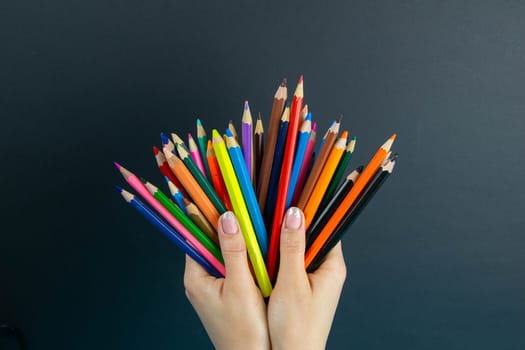 bunch of colored pencils in hand. A woman's hand holds a set of colored pencils on a black background.