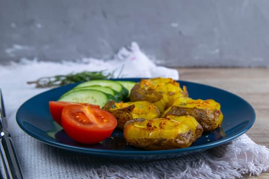 Baked potatoes with cheese, and salad with tomatoes and cucumbers on a blue plate.