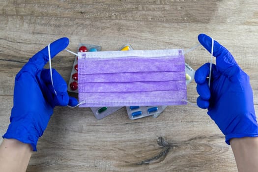 Doctor, nurse or scientist hand in blue nitrile gloves holding a medical face mask for protection against infection. Covid-19 coronavirus.