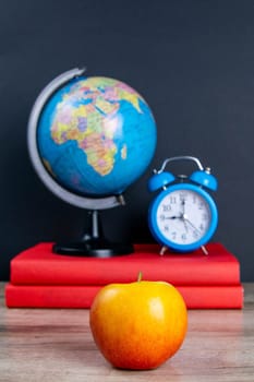The globe and the blue clock stand on a stack of books, next to an apple.