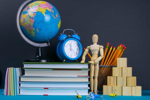 The globe and the clock stand on a stack of books, next to a glass of pencils and the pyramid is folded with wooden cubes and the figure of a wooden man.