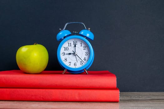 Blue watch and green apple stand on red books.
