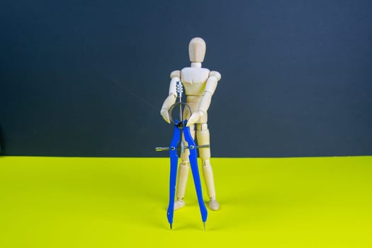 Wooden man figurine with compass on the yellow table.