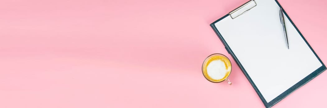 Tablet with a white sheet on which there is a silver pen and next to there is a glass with a coffe with milk.