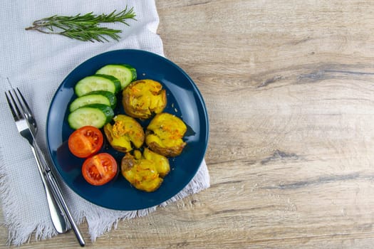 Baked potatoes with cheese, and salad with tomatoes and cucumbers on a blue plate.