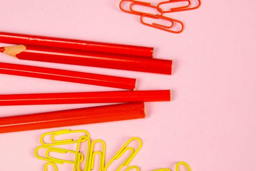 Multi-colored red pencils rulers, pens, pencils and scissors and stationery stand on a pink background.