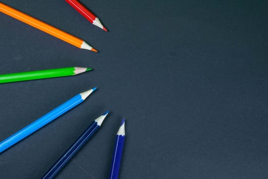 Colorful pencils arranged in a wave isolated over black background.