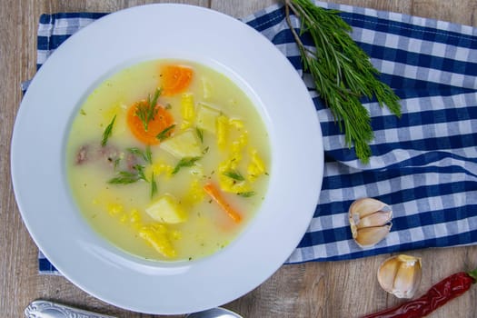 Potato cream soup with mushrooms, carrots and cheese. Top view. The plate stands on a checkered towel, next to a spoon.