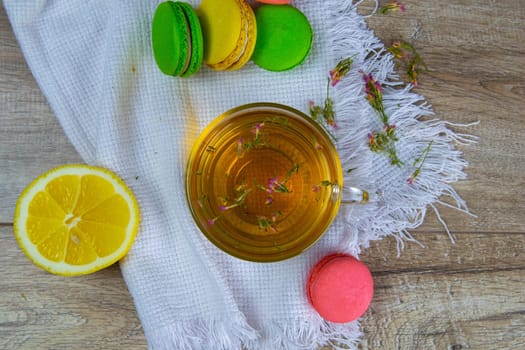 Glass transparent cup with mint tea stands on a wooden stand, next to a sugar bowl with sugar cubes, sliced lemon, spoon and multi-colored muffins.