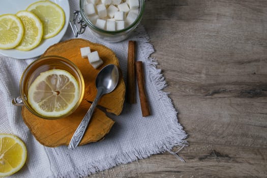 Glass transparent cup with mint tea stands on a wooden stand, next to a sugar bowl with sugar cubes, sliced lemon and a spoon.