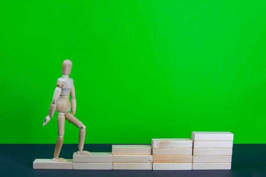 Wooden man walk up the career stairs. Ladder made with wooden bricks. Mannequin on top of development. Concept of personal development, career , changes, success. Green background, copy space for ad.