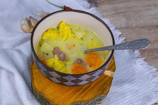 Potato cream soup with mushrooms, carrots and cheese. Top view. Soup in a brown plate, stands on a wooden stand, next to a hour, spoon, spices and lemon.