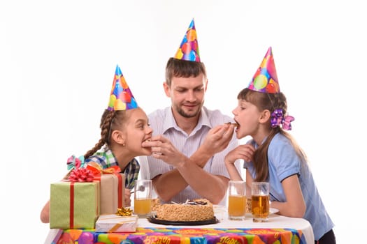 Kids bite pieces of cake from dad's hands, having fun celebrating a birthday