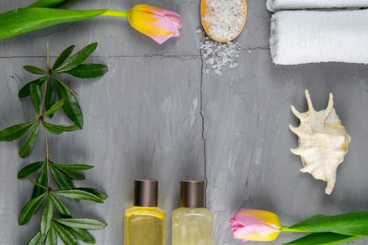 Two towels, body care oil, tulips, green branch and sea salt stand on a concrete background. Spa treatments concept, healthy body.