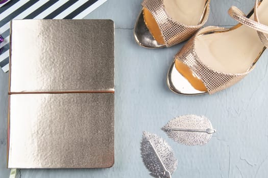 A gold notebook with women's shoes, tulips, glasses and a watch on a concrete background. Flet lay.