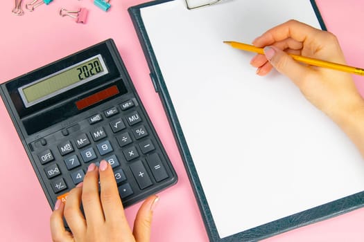 The hands of a woman count on a calculator and write notes. Top view of business woman's hands on white sheet. Finance and business concept.