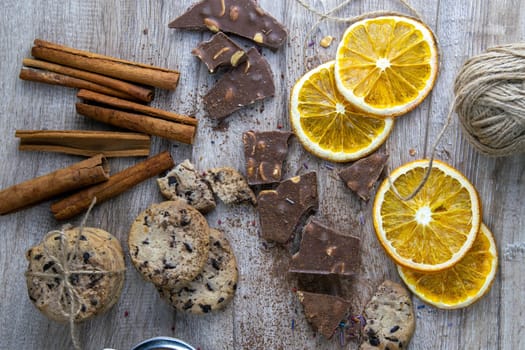 Dried oranges, chocolate slices, chocolate biscuits and cinnamon on a wooden table.