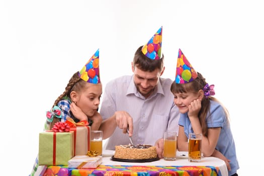 Dad and two daughters cut a birthday cake with a knife