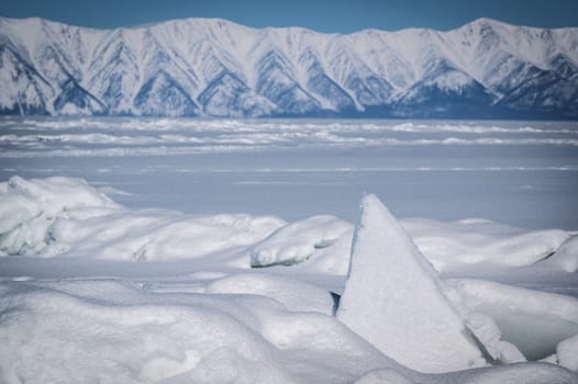 Transparent blue ice floes piled in ice hummocks against a blue sky on a sunny day. Unusual winter landscape of the frozen lake Baikal. Natural cold background. Siberia, Russia.