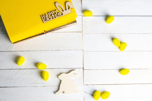 Yellow notepad with wooden rabbit, and yellow eggs on a white wooden table.