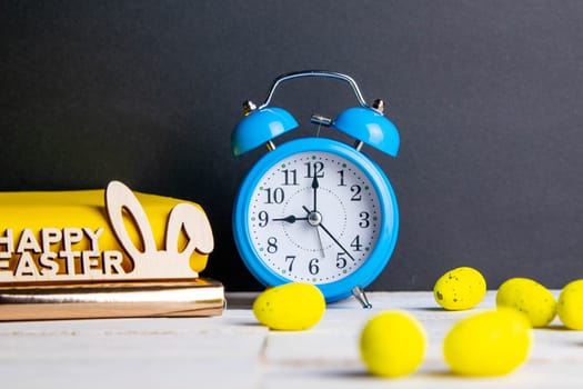 Easter concept, clock and apple, yellow books, eggs are scattered next to them, there is a wreath in the background.