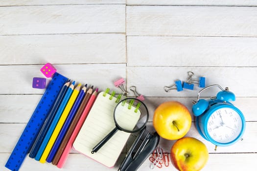 Various office stationery, notepad, clock, pencils, ooh, glasses, pen and two fresh apples on a white wooden table. Top view with copy space. Concept of office, education, workplace, school.