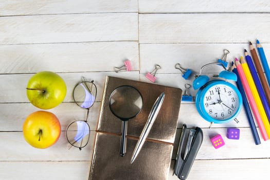 Various office stationery, notepad, clock, pencils, ooh, glasses, pen and two fresh apples on a white wooden table. Top view with copy space. Concept of office, education, workplace, school.