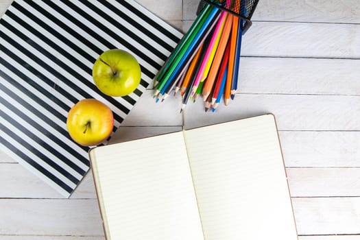 Top view of open notebook with empty pages, pencil and red apples on wooden table in office workspace.