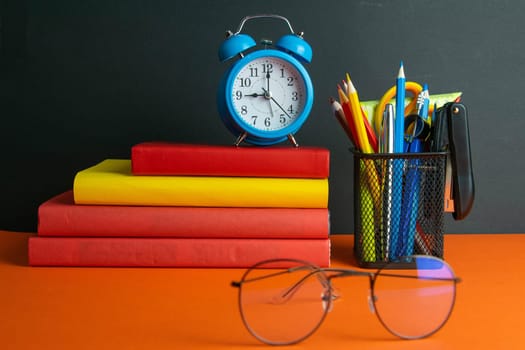 A stack of books, clock, world globe, and women's glasses in the foreground, stand on an orange background.