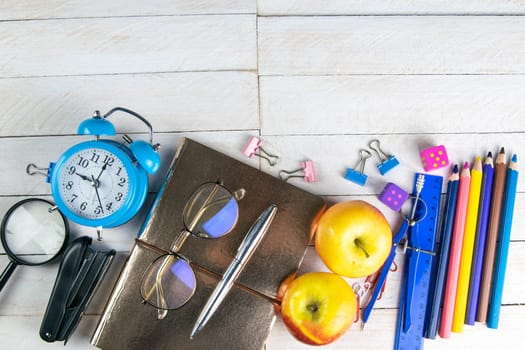 Various office stationery, notepad, clock, pencils, ooh, glasses, pen and two fresh apples on a white wooden table. Top view with copy space. Concept of office, education, workplace, school.